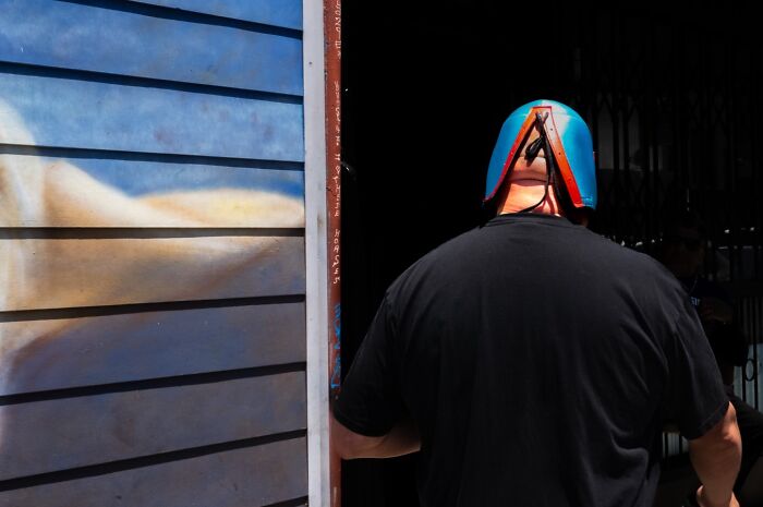 A photographer captures humor in everyday life: a man in a blue and orange helmet facing a dark doorway.