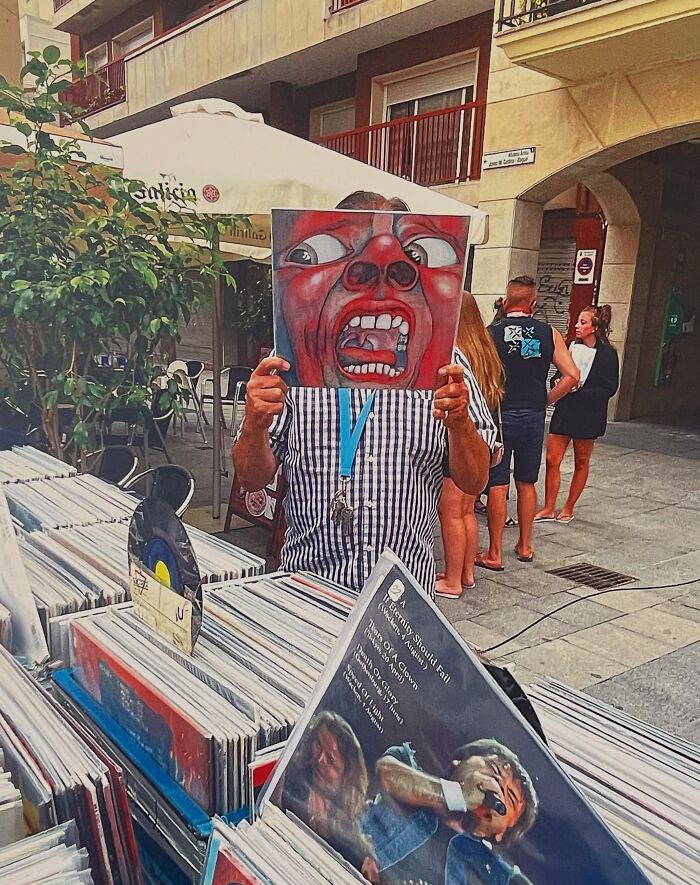 A photographer captures a perfectly timed coincidence of a man holding up a record album cover with a screaming face in Barcelona.