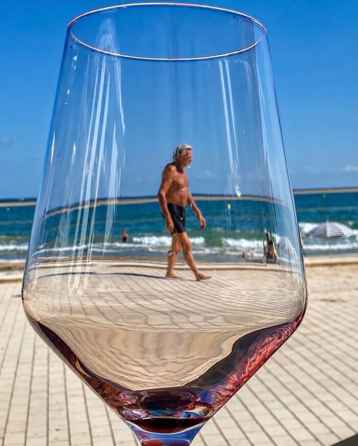 A photographer captures a perfectly timed coincidence of a man walking on a beach, perfectly framed through a wine glass in Barcelona.