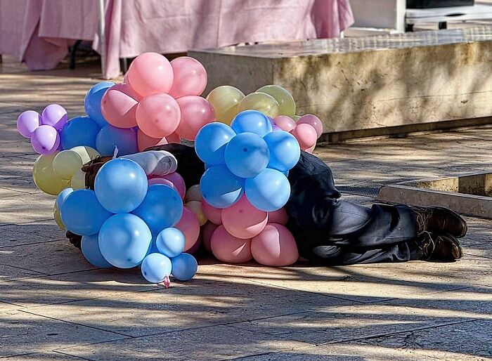 A person laying down on the street covered by pink and blue balloons, capturing perfectly timed coincidences in Barcelona.