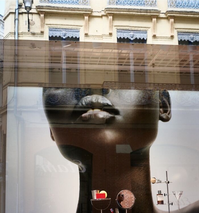Perfectly timed street photo showing a store display of a head with a building reflected, revealing an extraordinary moment.