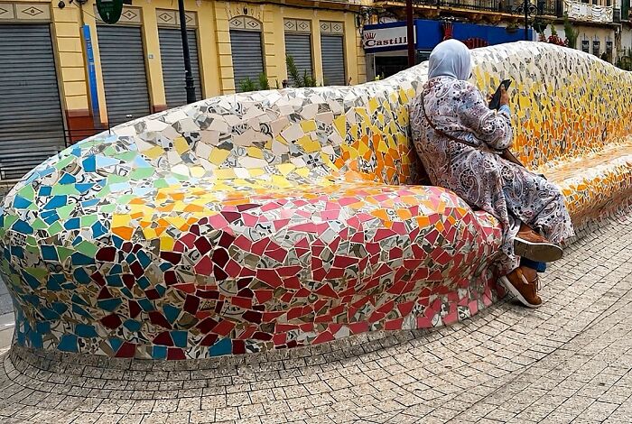 Woman in a hijab seated on a long, mosaic-tiled bench in Barcelona, a perfectly timed coincidence showing street life.