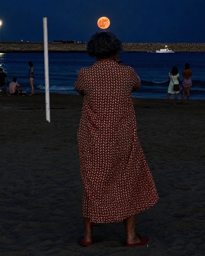 Woman on a beach in Barcelona, her head appearing to hold the moon, a perfectly timed coincidence.