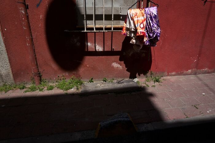 Perfectly timed street photo of clothes drying on a line against a red wall, creating an extraordinary moment with shadows.