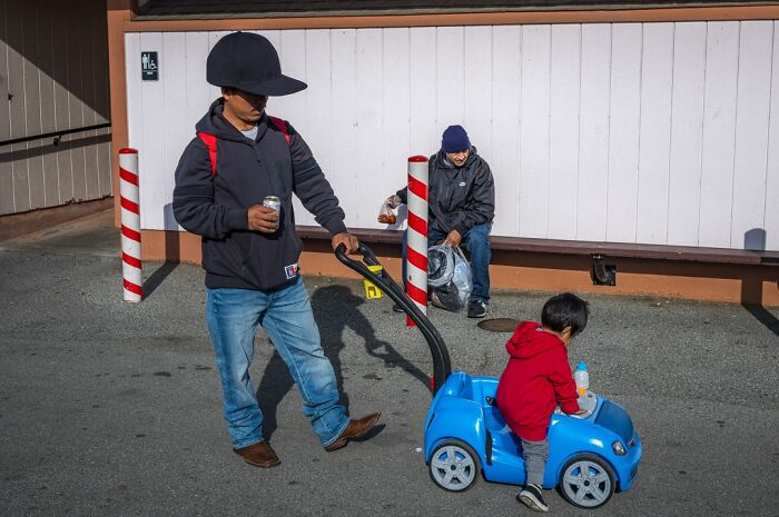 Photographer captures humor and chaos in everyday life, with a man pushing a child in a toy car.