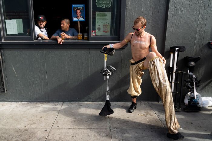 Photographer captures humor and chaos in everyday life, showing a man in gold pants with onlookers at a bar window.