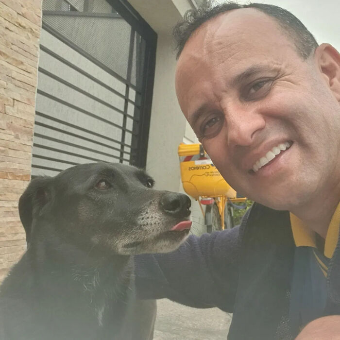 A kind mailman smiles, taking a selfie with a black dog sticking out its tongue, during his deliveries.