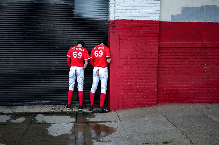 A photographer captures humor and chaos: two baseball players, CATCHER and PITCHER, urinating against a wall.