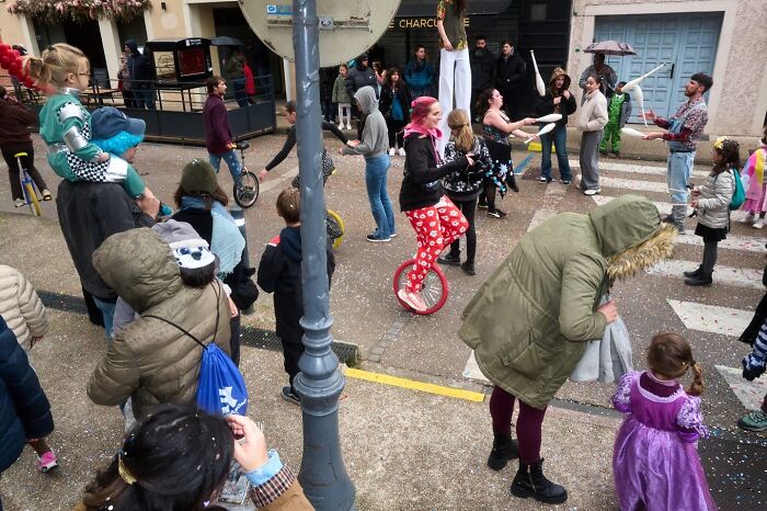 A perfectly timed street photo capturing a carnival street scene with jugglers, unicyclists, and spectators.