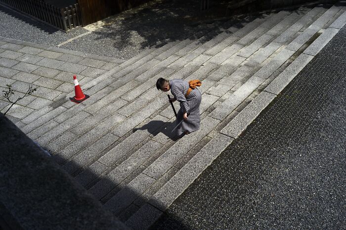 A perfectly timed street photo of a person in traditional attire with a cane on stone steps, revealing an extraordinary moment in everyday life.