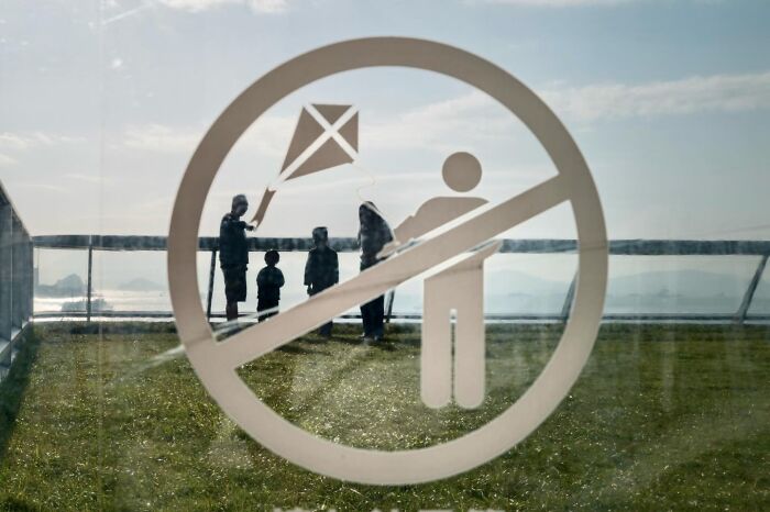 A no-kite-flying sign in the foreground, with people on a grassy area in the background, a street coincidence.