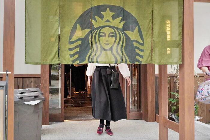 Street coincidences caught on camera by Edas Wong: A person standing in a doorway, their head obscured by a hanging Starbucks logo.