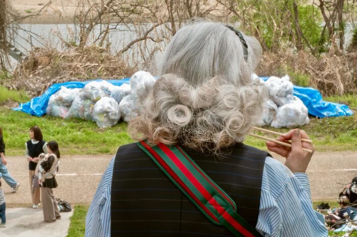 Street coincidences caught on camera by Edas Wong: An elderly person with curly white hair, holding chopsticks, perfectly matching a pile of white garbage bags in the background.