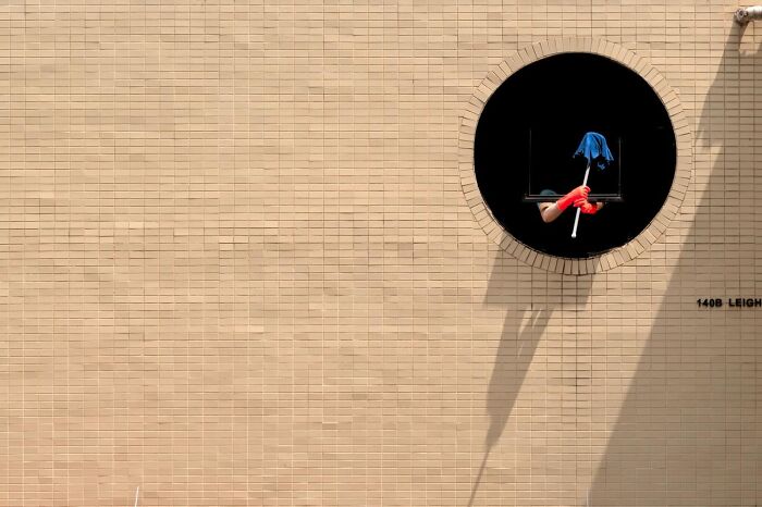 Street coincidences caught on camera: A person in a circular window holds a mop, casting a dramatic shadow on the building.