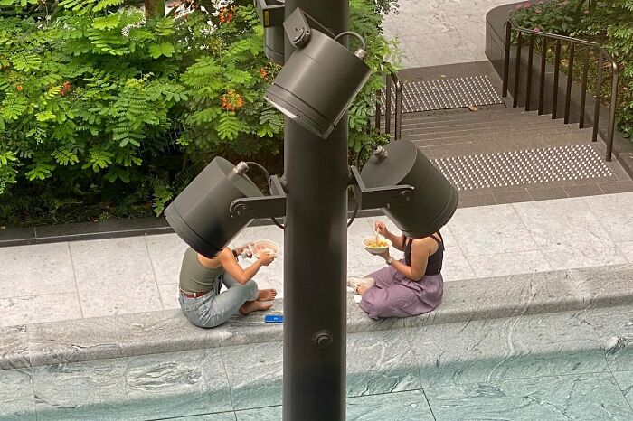 Two people eating noodles outdoors with large street lights perfectly positioned as hats, a street coincidence.