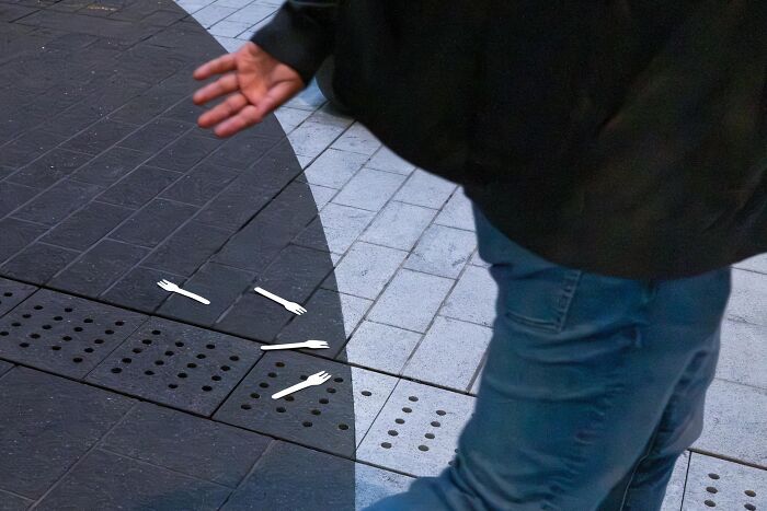 A man walking past several white plastic forks dropped on a dark gray gridded pavement, a street coincidence.