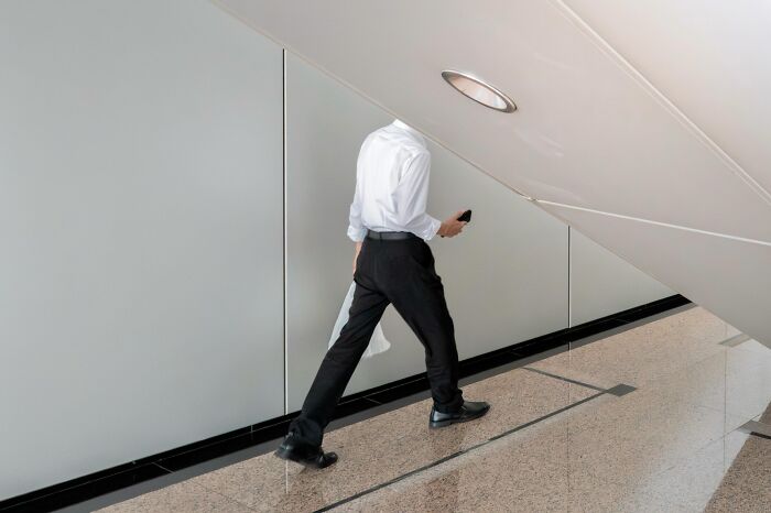 A man in a white shirt and black pants walks under an angled ceiling, making him appear headless, a street coincidence.