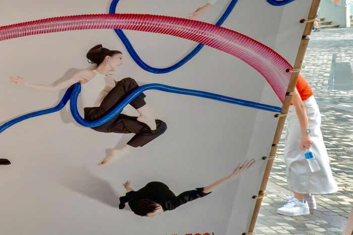 Street coincidences caught on camera: A person's leg aligns with a blue tube on a billboard, creating a humorous illusion.