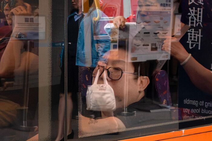 Street coincidences caught on camera: A person's reflection perfectly aligns with a small white bag on a bus window.