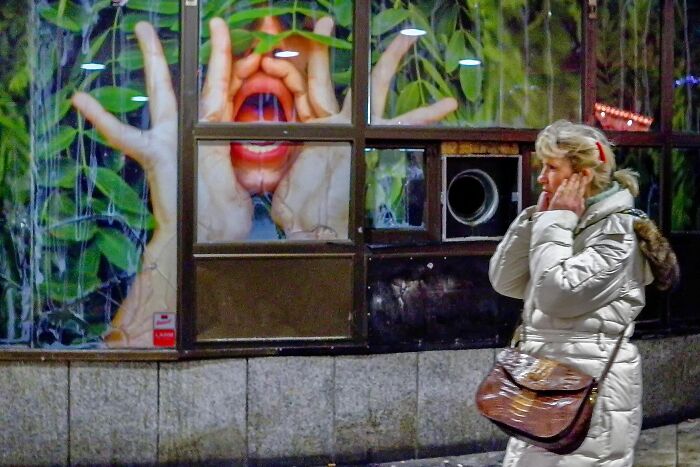 A woman walks past a window display with a large face illustration, creating a visual street coincidence.