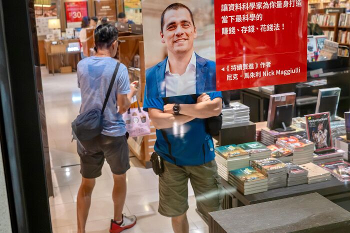A man in a blue shirt and shorts stands behind a cutout of another man, a funny street coincidence.