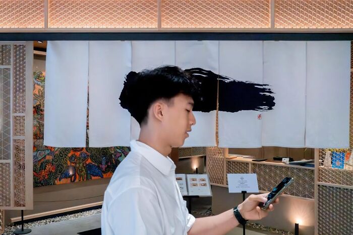 A man stands in front of a banner, a street coincidence where his hair aligns with a painted design.