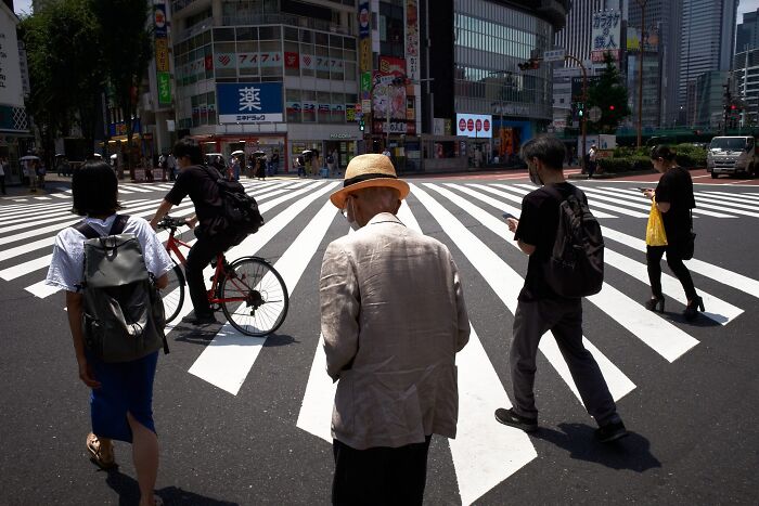 A perfectly timed street photo of pedestrians and a cyclist crossing a busy urban intersection, revealing an extraordinary moment in everyday life.