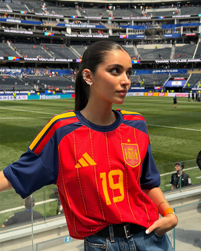 A woman, the World Cup hero's girlfriend, wearing a Spain soccer jersey in a stadium. A woman, the World Cup hero's girlfriend, wearing a Spain soccer jersey in a stadium.