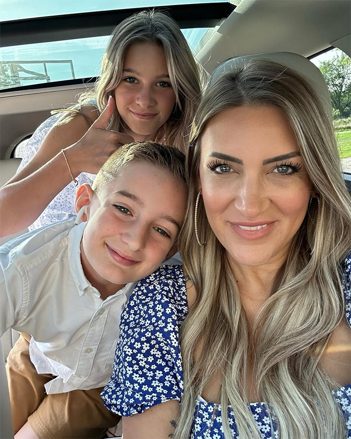 The influencer taking a selfie with her two children in a car, showing her family.