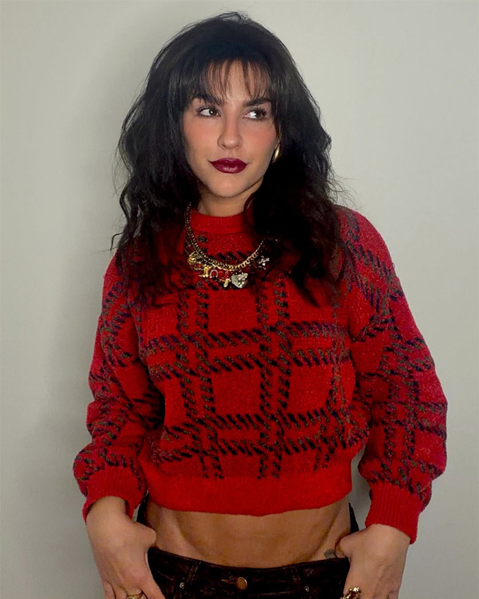 Influencer with dark hair and makeup in a red sweater, looking to the side. Featured in a video of influencer working out in a bikini.