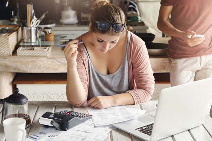 A young woman focused on paperwork, a calculator, and laptop, representing managing an inheritance or financial matters. A young woman focused on paperwork, a calculator, and laptop, representing managing an inheritance or financial matters.