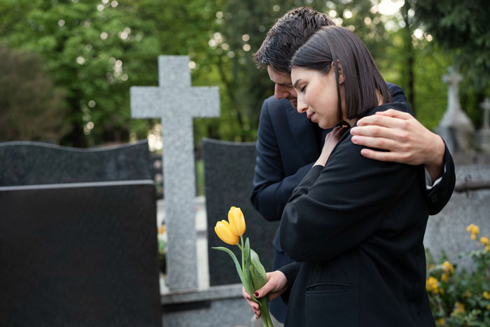 A person comforting another at a gravesite with yellow flowers, reflecting the inheritance and family dynamics. A person comforting another at a gravesite with yellow flowers, reflecting the inheritance and family dynamics.