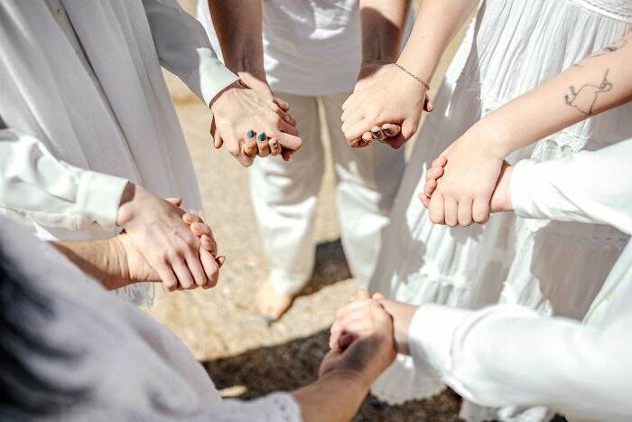 A group of people holding hands in a circle, dressed in white, representing the community aspect of cults.