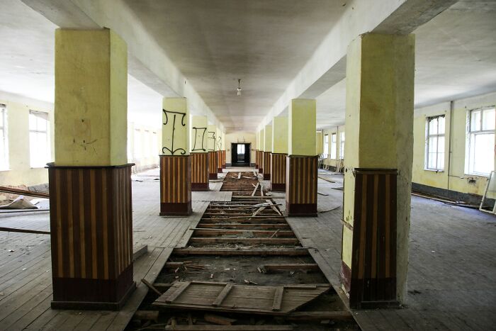 An abandoned hallway with broken floorboards and pillars, a setting for disturbing cults.