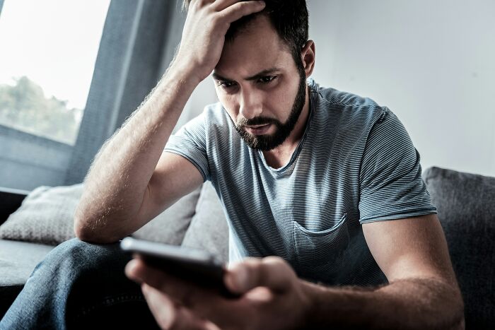 A distressed man looking at his phone, disturbed by internet rabbit holes or cults.