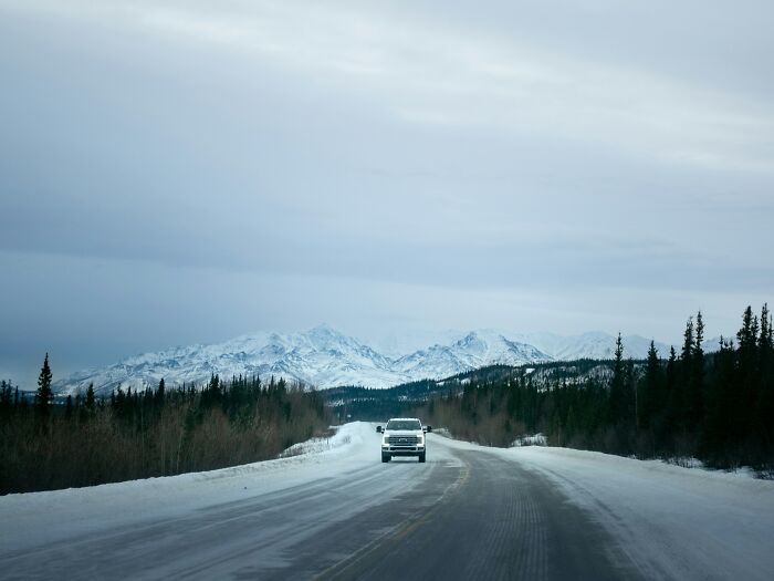 A vehicle drives on a snowy road with mountains in the background, a chilling internet rabbit hole.