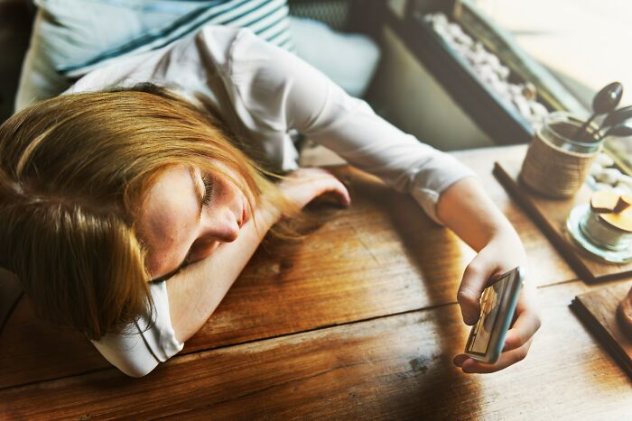 A person resting their head on a table while holding a phone, signifying deep dives into internet rabbit holes and cults.