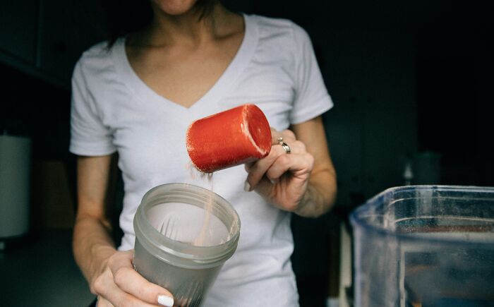 A person in a white t-shirt pouring a red scoop of powder into a shaker bottle, preparing a drink, symbolizing internet rabbit holes.