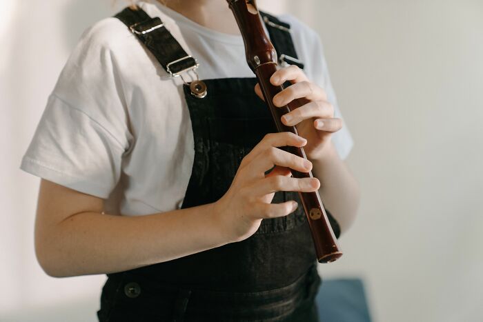 A person in black overalls and a white t-shirt playing a brown wooden flute, holding it with both hands, illustrating internet rabbit holes.