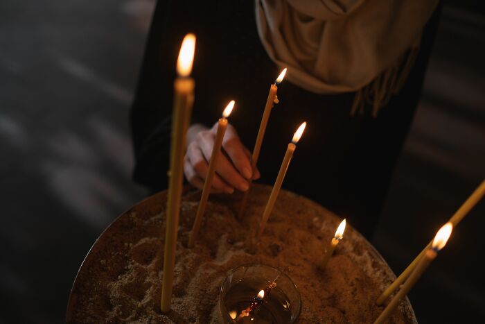 A person lighting candles in a dimly lit setting, symbolizing the spiritual or ritualistic side of cults.