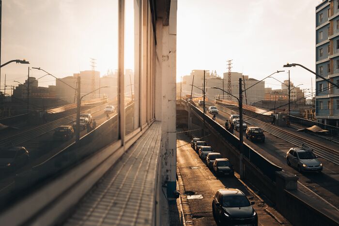 City street with cars and buildings reflecting in a window, evoking the unsettling feel of cults and internet rabbit holes.