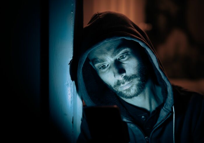 A man in a hooded sweatshirt looking at his phone, potentially disturbed by internet rabbit holes or cults.