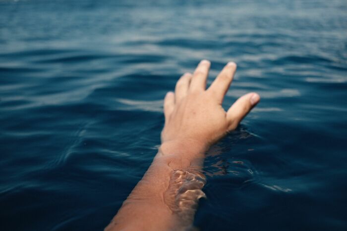 A hand reaching out of dark blue water, symbolizing being deeply disturbed by cults.