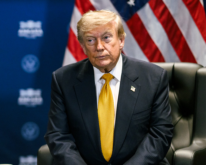 Trump, in a suit and yellow tie, sits with a serious expression, with the American flag visible in the background. Trump, in a suit and yellow tie, sits with a serious expression, with the American flag visible in the background.