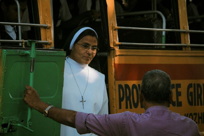 A nun looking out from a bus, possibly experiencing mansplaining examples from the man in the foreground.