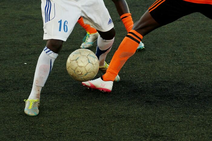 Two soccer players' legs are close to a ball on a green field, representing the spirit of micro feminism.