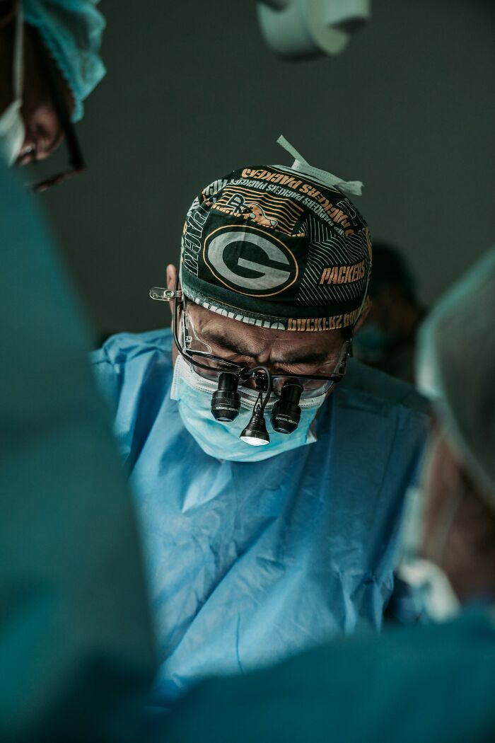 A surgeon in a green cap and mask, with magnifying glasses, performs a procedure, avoiding medical mistakes.