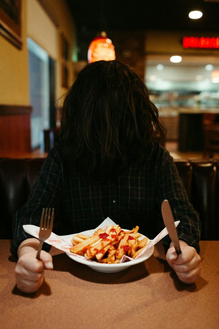 A person with long dark hair covering their face, sitting at a table with a plate of french fries, representing unsolved mysteries.