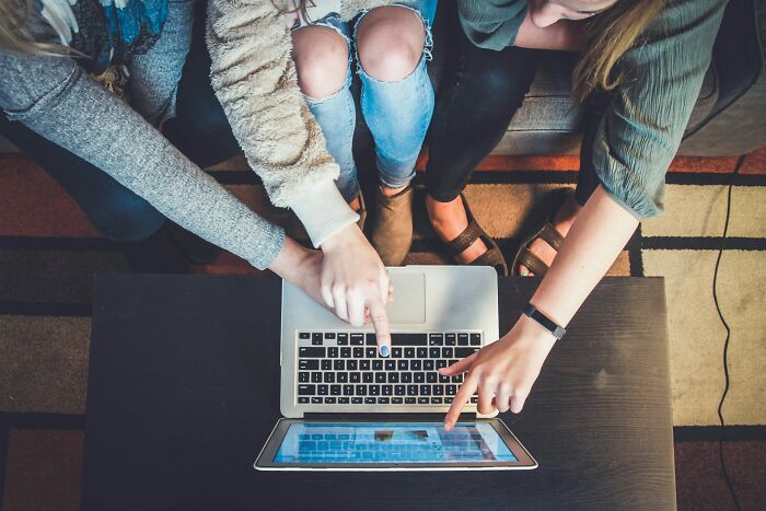 Three people pointing at a laptop and tablet, showing micro feminism clap backs on screen, from a top-down perspective.
