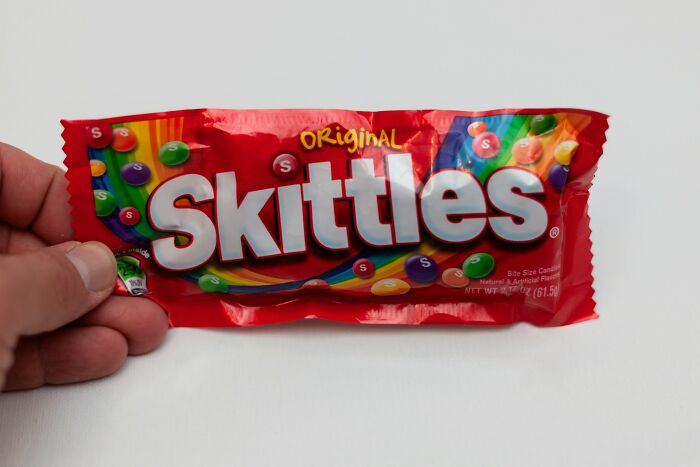 A hand holds a bag of Skittles candy, a common item found in many babysitting stories.